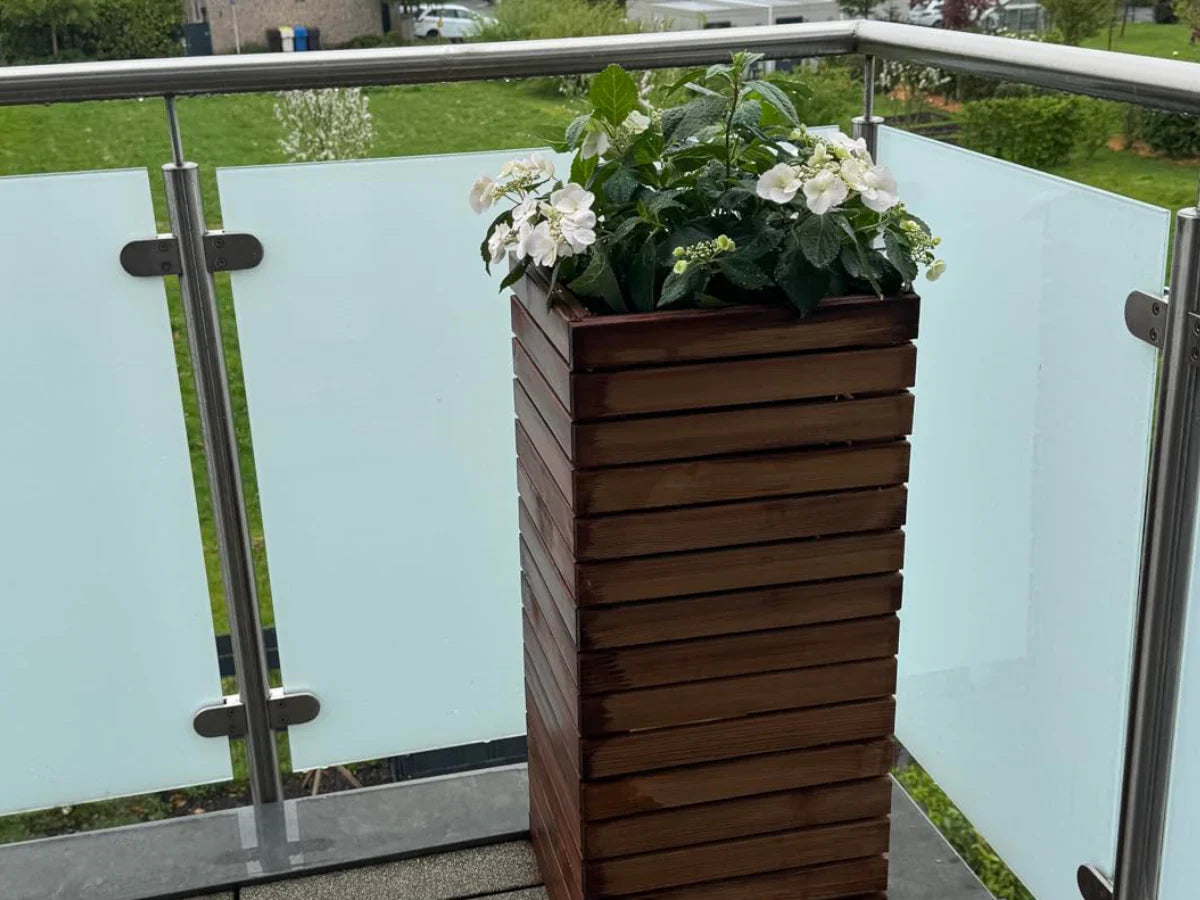 Drewniana donica z białymi kwiatami na balkonie z przeszkloną balustradą