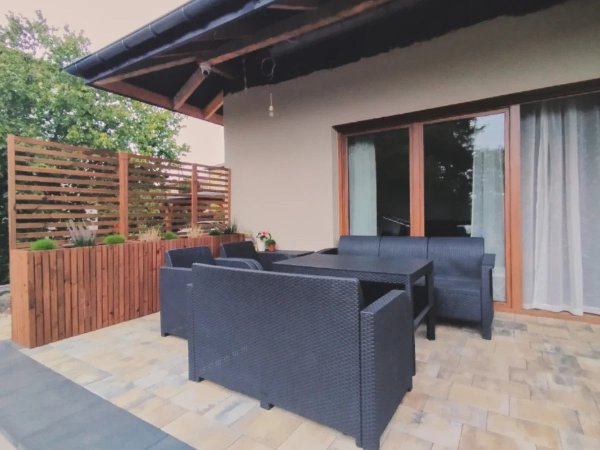 Taras z meblami ogrodowymi, dużą donicą i pergolą z drewna, przy nowoczesnym domu