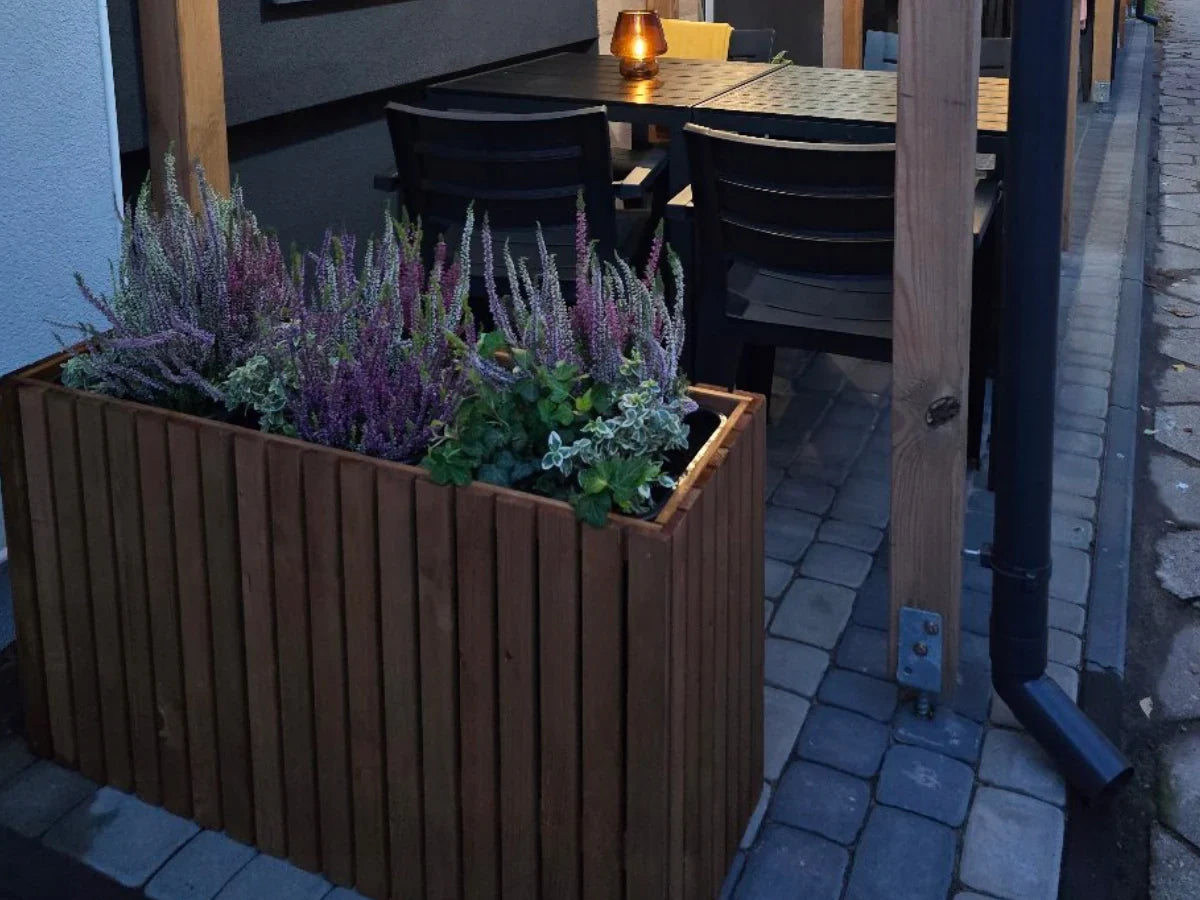 Drewniana donica z wrzosami na tarasie obok stołu i krzeseł na kostce brukowej