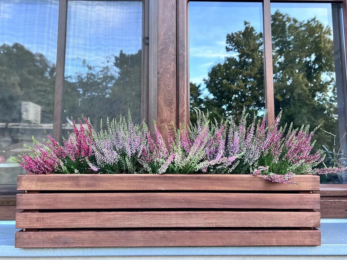 Drewniana donica z naturalnymi wrzosami przed oknem, donice ogrodowe z drewna