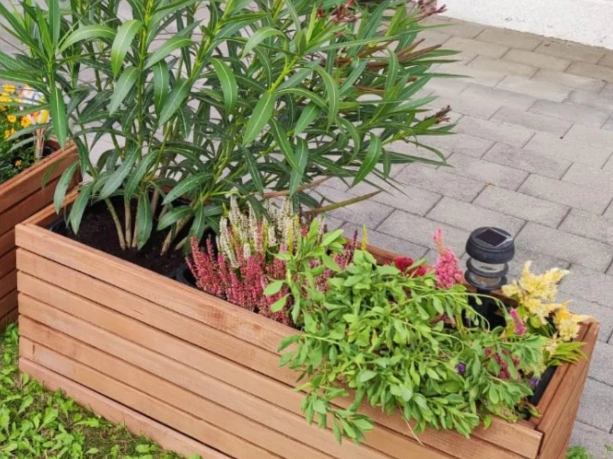 Drewniana donica ogrodowa z kolorowymi roślinami i lampą solarną na tarasie