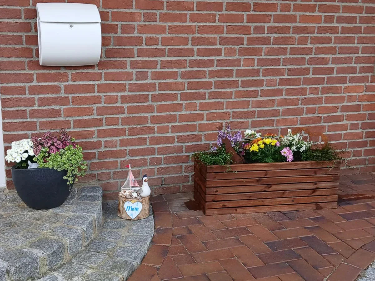 Drewniana donica prostokątna z kolorowymi kwiatami na tle ceglanej ściany, dekoracja ogrodowa