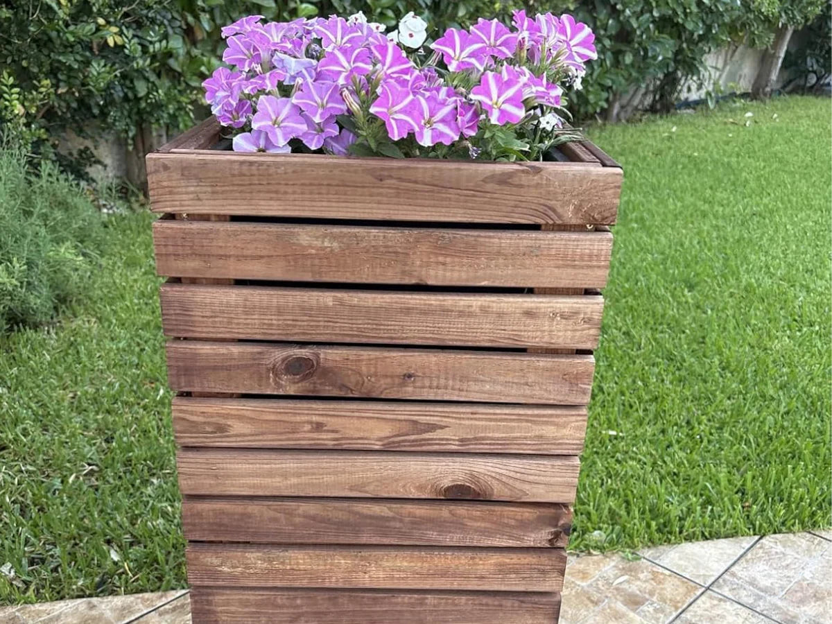 Drewniana donica ogrodowa z fioletowymi kwiatami na tle trawnika