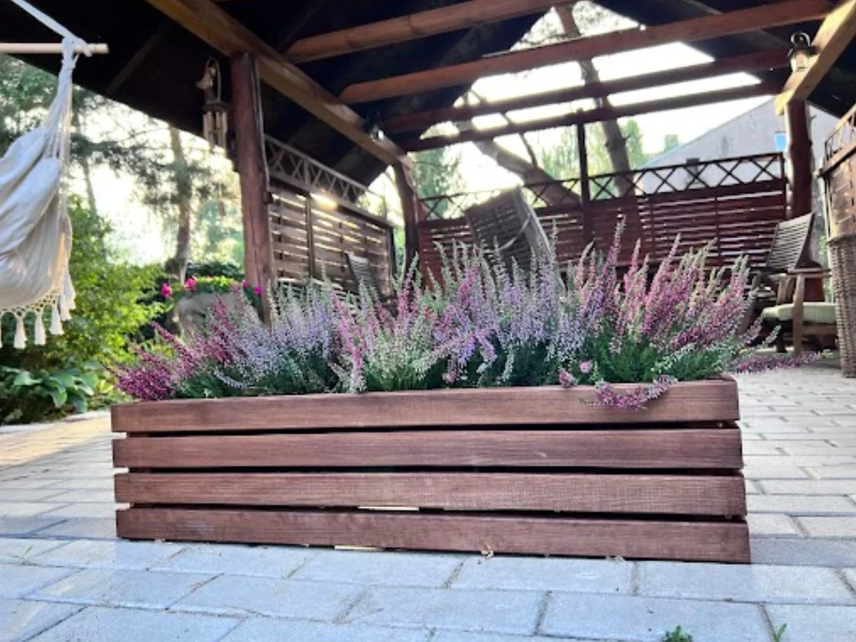 Duża drewniana donica z wrzosami na tarasie, pod zadaszeniem ogrodowym