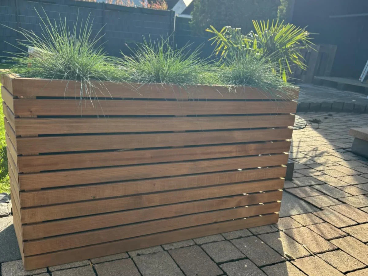Duża donica ogrodowa z drewna z trawami i palmą na tarasie, trwałe donice drewniane